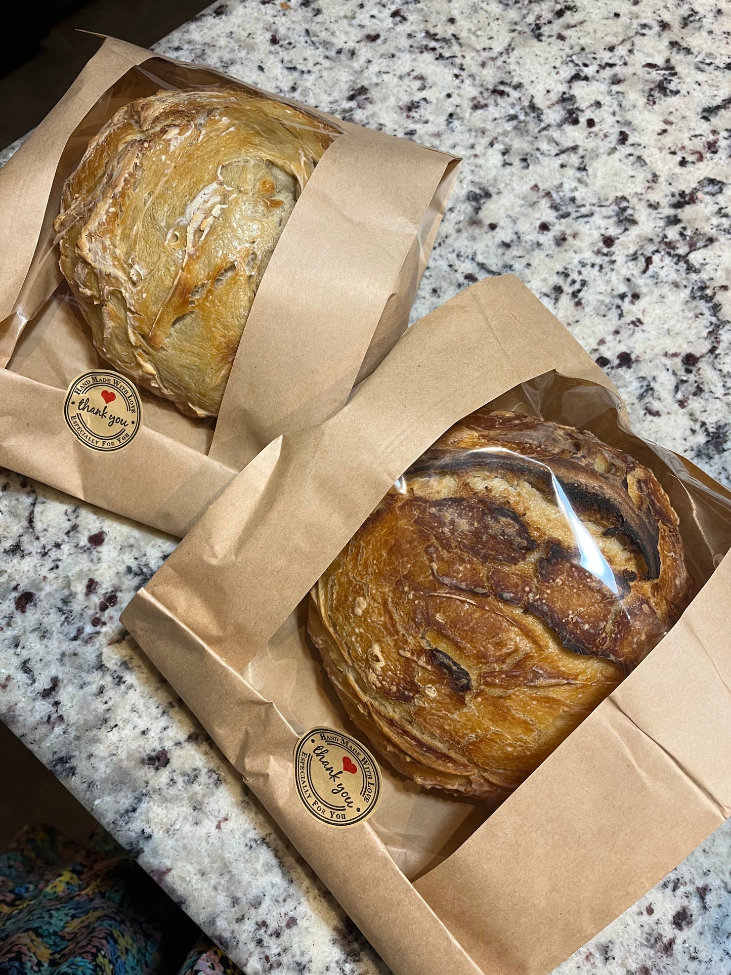 Two loaves of bread in brown paper packaging on a marble countertop.